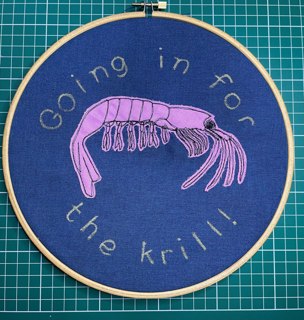 Pink sewn krill on blue fabric with text Going in For the Krill